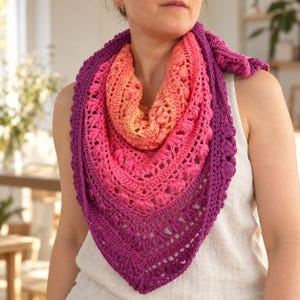 May include: A triangular crochet shawl featuring a vibrant gradient color transition from bright orange at the neckline to deep purple at the bottom point. The accessory is crafted with a textured stitch pattern incorporating small puff clusters.