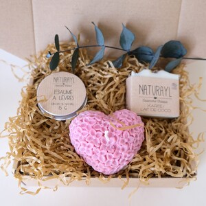 K&ouml;nnte beinhalten: Eine Geschenkbox gef&uuml;llt mit braunem Packpapier und einer rosa herzf&ouml;rmigen Kerze. Die Box enth&auml;lt auch ein kleines Glas Lippenbalsam mit der Aufschrift "NATURAYL Baume a Levres 15g" und eine Seife mit der Aufschrift "NATURAYL Savonnerie Chaste Karite/ Lait de Coco".