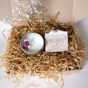 K&ouml;nnte beinhalten: Eine Geschenkbox gef&uuml;llt mit braunem Packpapier, einer wei&szlig;en Kerze mit getrockneten Blumen und einer Seife mit dem Text "NATURAYL Savonnerie Creative KARITE/ LAIT DE COCO".