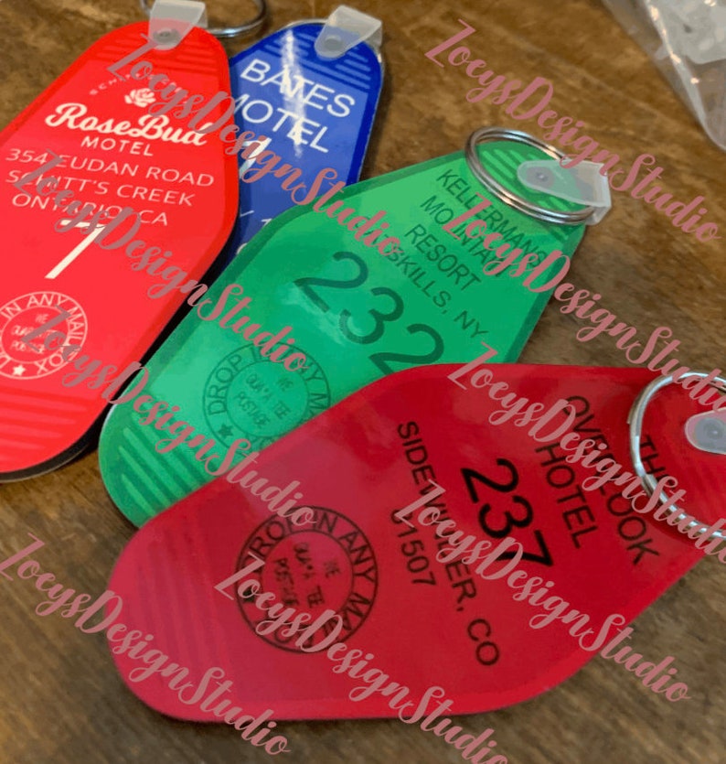 May include: A collection of vintage-style hotel keychains in red, green, and blue. The keychains feature hotel names and room numbers, with text including "Rose Bud Motel," "Bates Hotel," "Kellermans Resort," and "The Overlook Hotel."