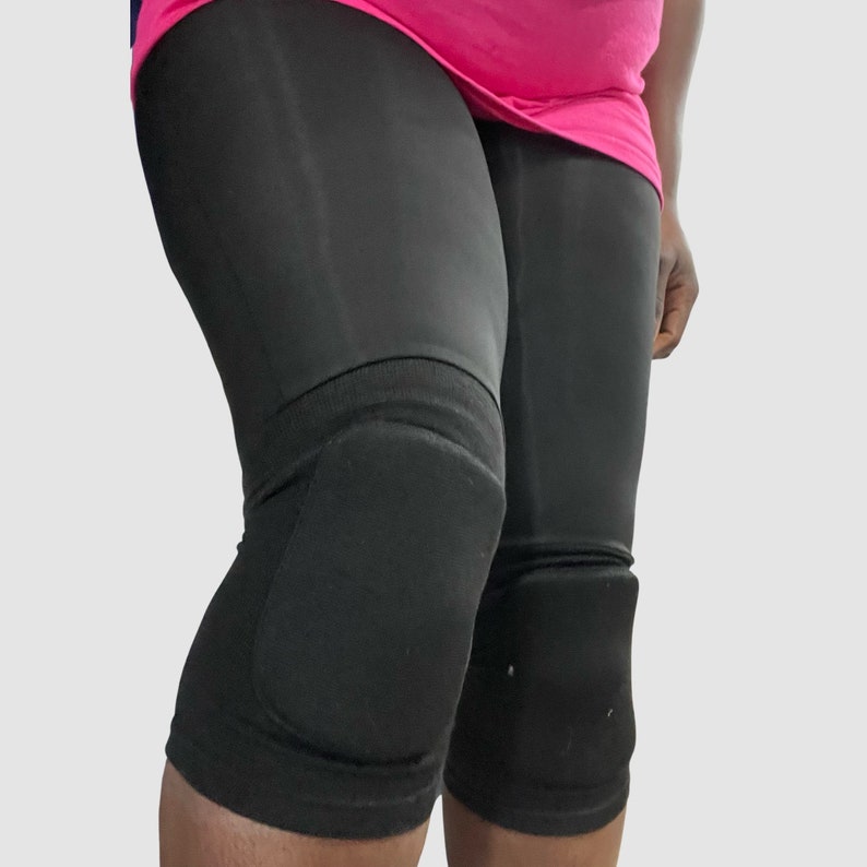 Op de afbeelding: Zwarte kniebeschermers met een dikke laag padding. De kniebeschermers worden gedragen over een zwarte legging.