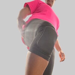 Op de afbeelding: Een persoon draagt ​​zwarte sport shorts met een kniebeschermer op het rechterbeen en een roze t-shirt.