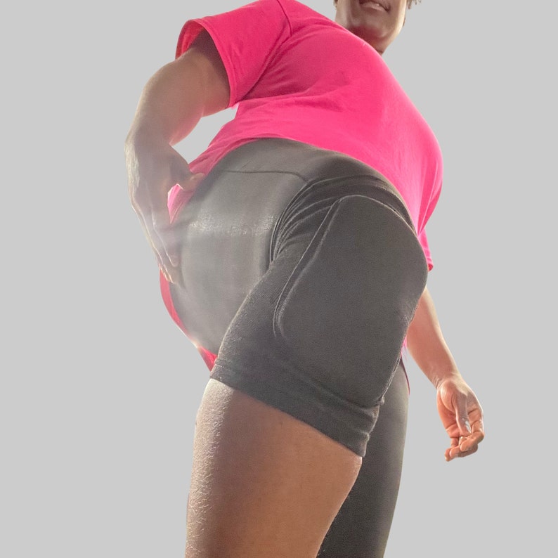 Op de afbeelding: Een persoon draagt ​​zwarte sport shorts met een kniebeschermer op het rechterbeen en een roze t-shirt.