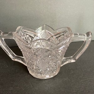 May include: A clear glass sugar bowl with two handles. The bowl has a cut glass design and is in good condition.