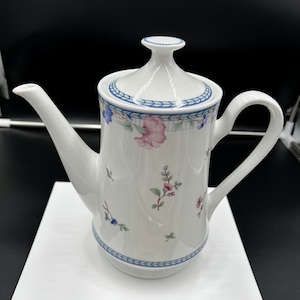 May include: White porcelain coffee pot with a floral design in shades of pink, blue, and green. The pot has a lid and a handle.