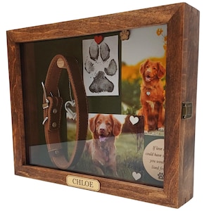 May include: A rectangular wooden shadow box frame with a dark brown finish, featuring a glass front. Inside, a brown leather dog collar, a paw print, two photographs of a golden-colored dog, and a plaque with the name CHLOE are displayed.