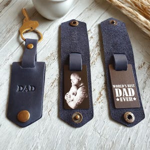 May include: Three leather keychains with different designs. The first keychain has the word "DAD" embossed on it. The second keychain has a photo of a man holding a baby. The third keychain has the text "WORLD'S BEST DAD EVER" on it.