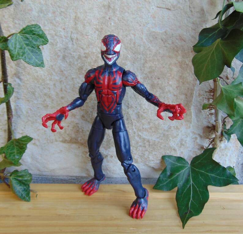 May include: A blue and red action figure of a character with a menacing grin. The figure has a red spiderweb design on the chest and arms, with red claws and feet. The figure is posed with arms outstretched.