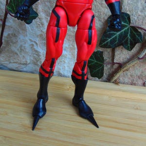May include: Close-up of a red and black action figure's legs. The figure has black boots with pointed toes.