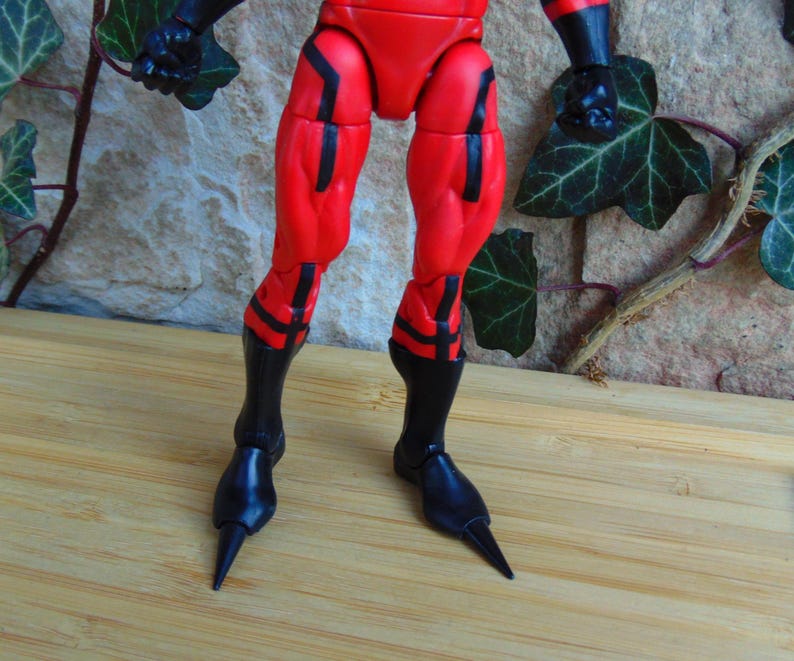 May include: Close-up of a red and black action figure's legs. The figure has black boots with pointed toes.