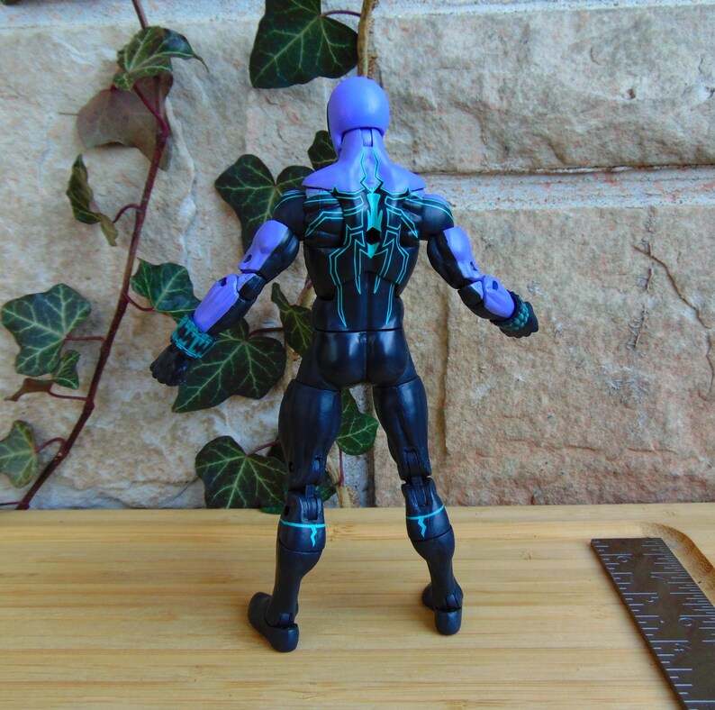 May include: Black and purple action figure with a green spider design on the back. The figure is posed with arms outstretched and legs slightly apart.