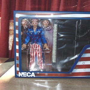 Action figure di Elton John del 1976 "Louder than Concorde", con abito in tessuto e pianoforte a coda in scala, oggetto da collezione.