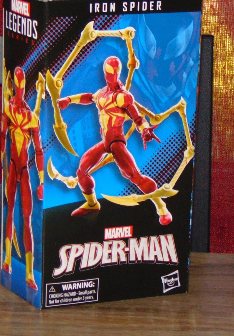 Pu&ograve; includere: Action figure di Iron Spider Marvel Legends in scatola. La figura &egrave; rossa e gialla con molteplici zampe di ragno meccaniche. La scatola presenta il logo Marvel Spider-Man e un'avvertenza per le piccole parti.