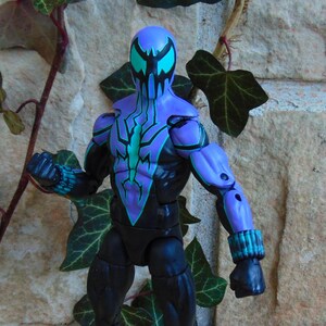May include: A black and purple action figure of a superhero wearing a mask with blue and black accents. The figure is posed with one arm raised and the other arm bent at the elbow.