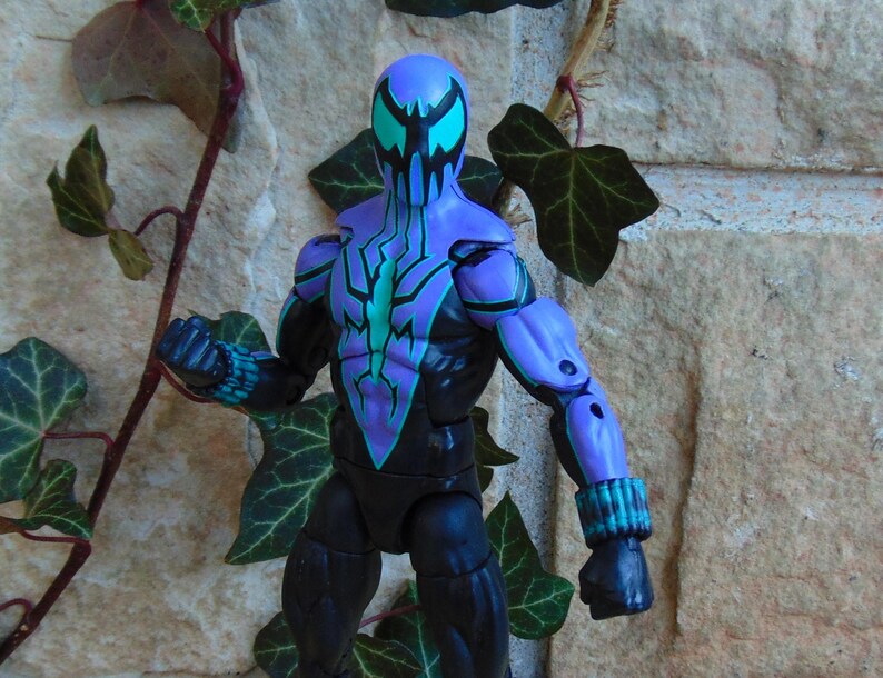 May include: A black and purple action figure of a superhero wearing a mask with blue and black accents. The figure is posed with one arm raised and the other arm bent at the elbow.