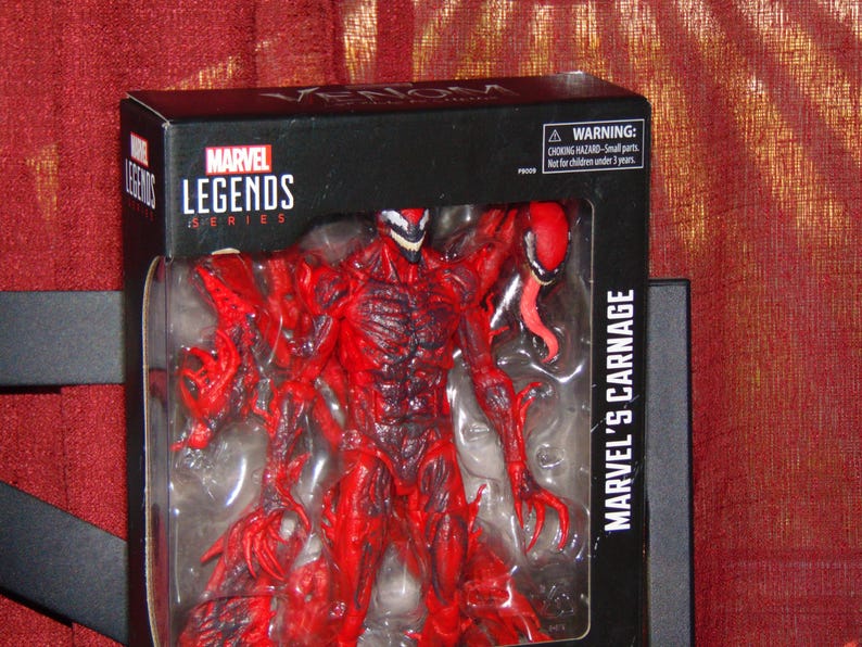 May include: A Marvel Legends action figure of Marvel's Carnage, a red and black character with a long tongue, in its original packaging. The box is black with the Marvel Legends Series logo and the text "MARVEL'S CARNAGE".