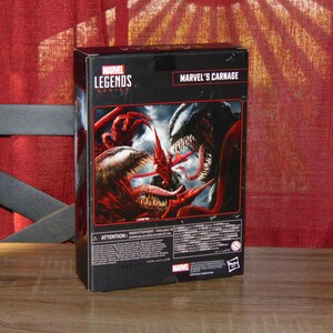 May include: A Marvel Legends Series action figure box featuring Marvel's Carnage. The box has a black background with images of Carnage in red and white. The Marvel Legends Series logo is visible.
