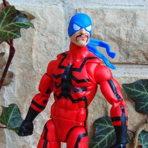 May include: A red and black action figure with a blue mask and a blue bandana. The figure has a black spider design on the chest.