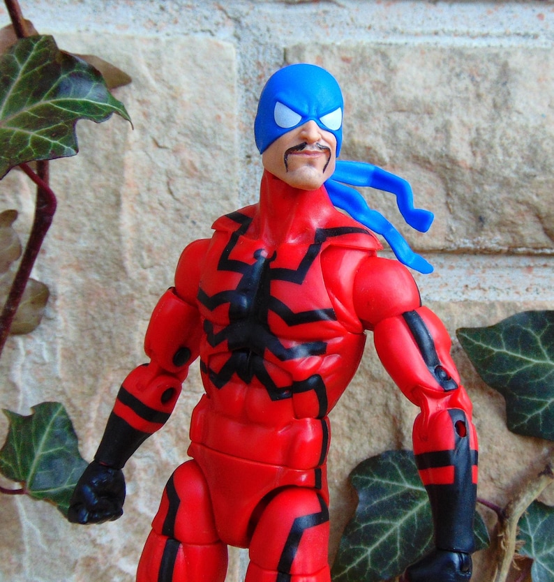 May include: A red and black action figure with a blue mask and a blue bandana. The figure has a black spider design on the chest.