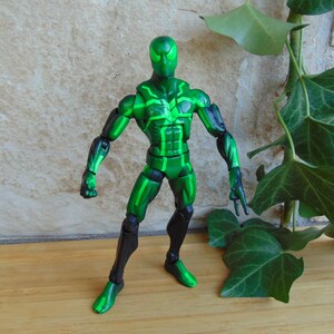 May include: A green action figure with black accents. The figure has a superhero-like design with a mask and a detailed pattern of green lines across the body. The figure is posed in a standing position.