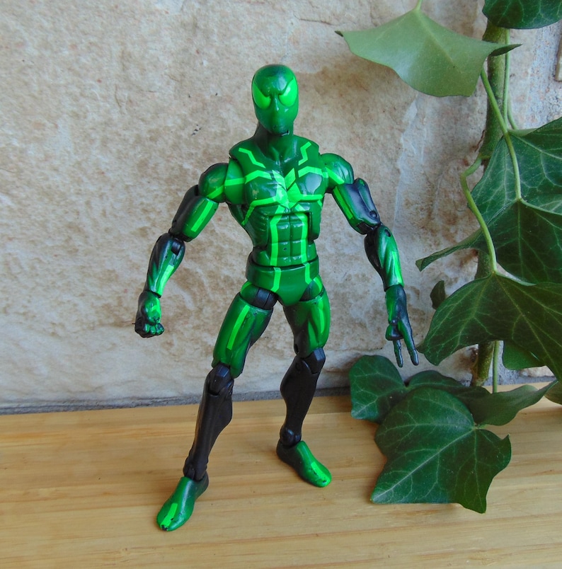 May include: A green action figure with black accents. The figure has a superhero-like design with a mask and a detailed pattern of green lines across the body. The figure is posed in a standing position.