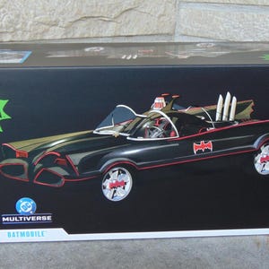 May include: A black box featuring a detailed illustration of the Batmobile from the Batman Classic TV Series. The Batmobile is black with red accents and the Batman logo. The box also displays the Batman logo and the text "BATMAN CLASSIC TV SERIES".
