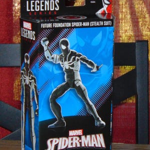 May include: A Marvel Legends action figure box featuring Future Foundation Spider-Man (Stealth Suit). The box is predominantly black and blue, with a dynamic illustration of the character. The Marvel Spider-Man logo is prominently displayed.