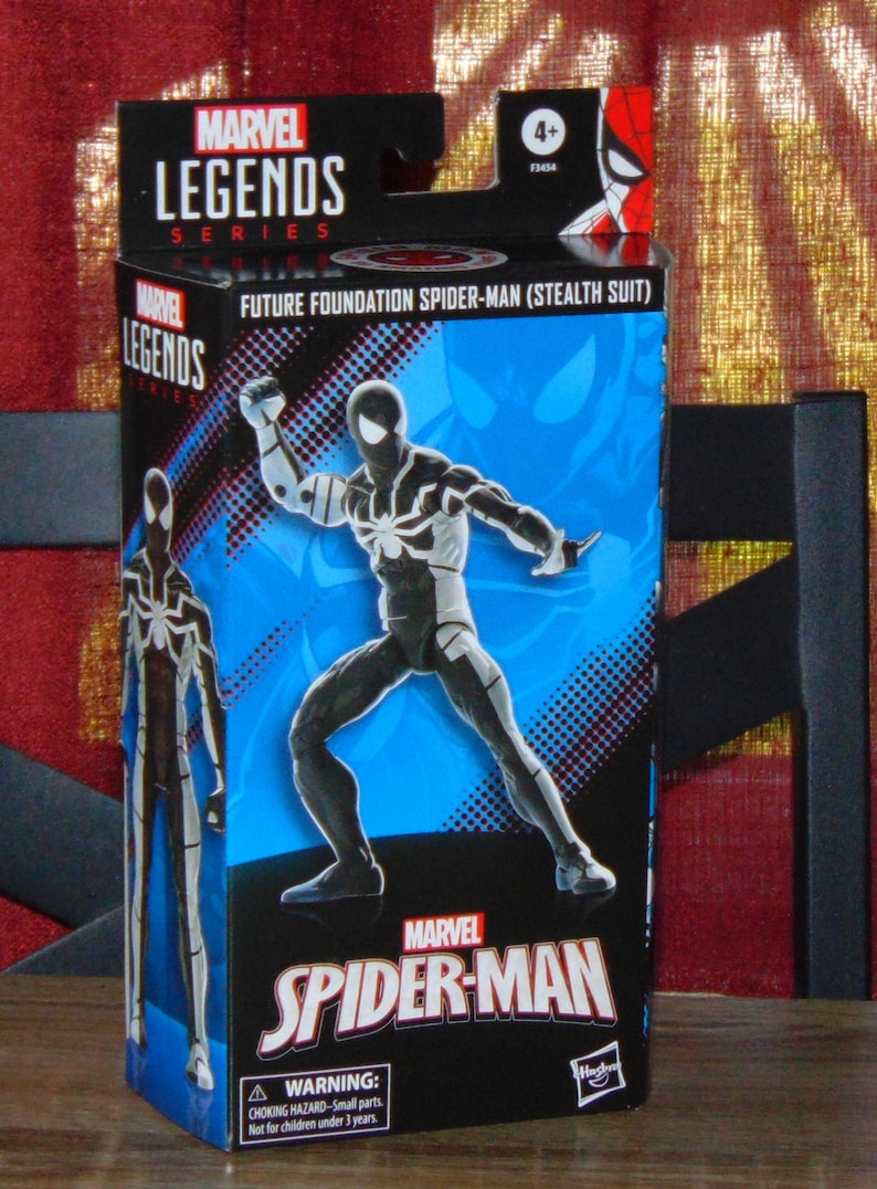 May include: A Marvel Legends action figure box featuring Future Foundation Spider-Man (Stealth Suit). The box is predominantly black and blue, with a dynamic illustration of the character. The Marvel Spider-Man logo is prominently displayed.