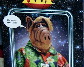 Può includere: Alf, l'alieno della popolare serie televisiva degli anni '80, indossa una camicia hawaiana colorata e un badge che dice "Melmac Cosmic Con Intergalactic". È in piedi davanti a uno sfondo stellato.