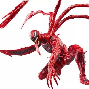 May include: A red action figure of the Marvel Comics character Carnage, in a crouching pose. The figure has a detailed, textured appearance with multiple tendrils extending from its back. The figure's face features a white and black mask, a long red tongue, and sharp teeth.