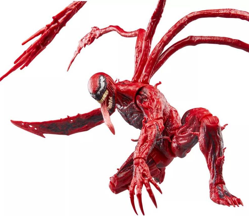 May include: A red action figure of the Marvel Comics character Carnage, in a crouching pose. The figure has a detailed, textured appearance with multiple tendrils extending from its back. The figure's face features a white and black mask, a long red tongue, and sharp teeth.