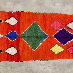 May include: A rectangular rug with an orange background and a pattern of colorful diamonds. The diamonds are in shades of black, white, blue, green, purple, pink, and yellow.