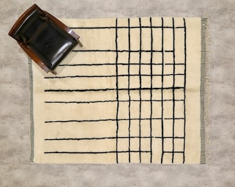 Op de afbeelding: Een wit tapijt met een zwart geometrisch patroon. Het patroon is een raster van horizontale en verticale lijnen.