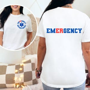 May include: White t-shirt with a blue and red "EMERGENCY" graphic on the back and a blue star of life graphic inside a circle with the text "EMERGENCY DEPARTMENT" on the front.