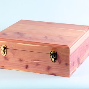 May include: A wooden box with a natural cedar finish and brass clasps. The box is closed and has a smooth, polished surface.