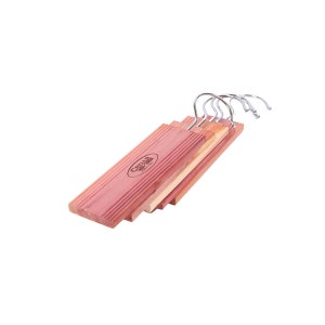May include: A set of four cedar wood hangers with metal hooks. The hangers are stacked on top of each other and have a natural cedar wood finish. The hangers are branded with the text "Cedar Fresh" in a white oval.