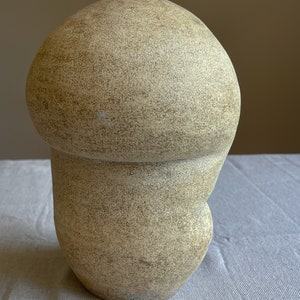Puede incluir: Una escultura beige con forma de hongo y superficie texturizada. La escultura tiene una parte superior redondeada y una base bulbosa, creando una forma org&aacute;nica &uacute;nica. El color neutro y el dise&ntilde;o sencillo la convierten en una pieza decorativa vers&aacute;til.