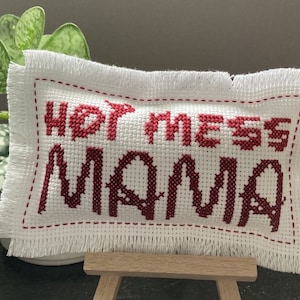 May include: White pillow with a red embroidered message that says "Hot Mess Mama".