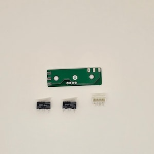 Może przedstawiać: Zielona płytka drukowana z białym złączem, dwoma czarnymi przełącznikami typu „toggle” oznaczonymi jako „D2F-D1FL” oraz białym złączem z sześcioma pinami.