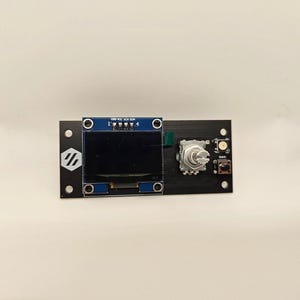May include: A black circuit board with a blue screen, a silver knob, and a small black button. The text "GND VCC SDA SCL" is printed on the board.