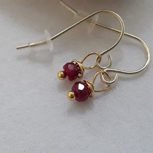 May include: A pair of silver earrings with small red gemstone beads and gold accents.