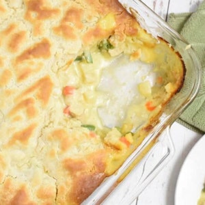 May include: A glass baking dish filled with a golden-brown baked casserole. The casserole has a flaky crust and a creamy filling with visible pieces of vegetables. A portion has been removed, revealing the filling.