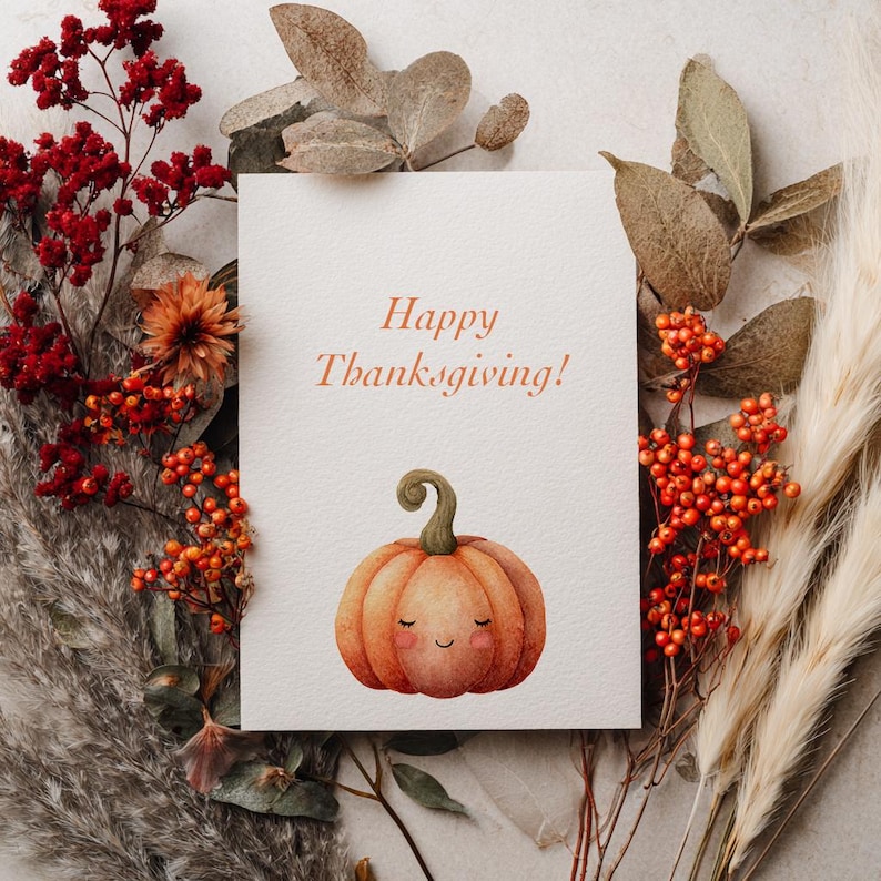 May include: A greeting card with the text "Happy Thanksgiving!" and a watercolor illustration of a smiling pumpkin. The card is surrounded by fall foliage, including red berries, dried leaves, and feathery grasses, creating a seasonal arrangement.