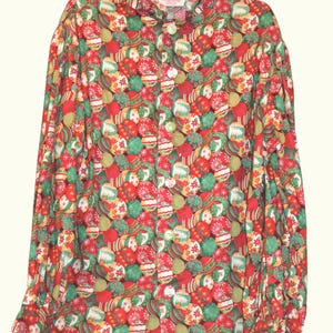 May include: A long-sleeve button-down shirt featuring a vibrant all-over print of red, green, and gold Christmas ornaments. The pattern includes various spherical designs with intricate snowflake and striped details on a light-colored fabric base.