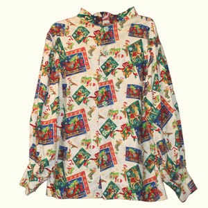 May include: A long-sleeved button-down shirt featuring an off-white background with a repeating Christmas-themed print. The pattern includes illustrations of reindeer, sleighs, stockings, and candy canes in red, green, blue, and gold colors.