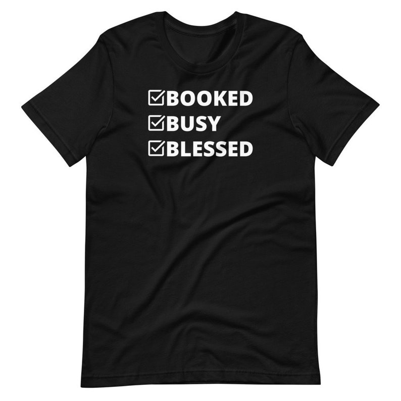 K&ouml;nnte beinhalten: Schwarzes T-Shirt mit wei&szlig;em Text, der "BOOKED BUSY BLESSED" lautet, mit H&auml;kchen neben jedem Wort.