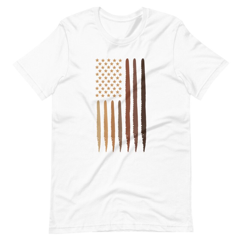 Op de afbeelding: Wit T-shirt met een afbeelding van een Amerikaanse vlag. De vlag is gemaakt van verschillende bruintinten, die verschillende huidtinten voorstellen. De sterren zijn goudkleurig.