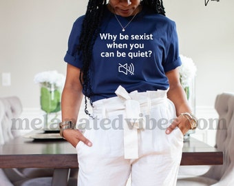 Könnte beinhalten: Ein marineblaues T-Shirt mit dem Text "Why be sexist when you can be quiet?" und einem Stumm-Symbol. Das Shirt wird von einer Person mit einem breitkrempigen Hut und einer weißen Hose getragen.