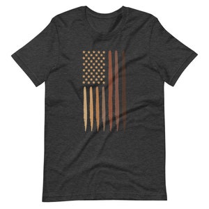 Op de afbeelding: Een donkergrijs t-shirt met een afbeelding van een Amerikaanse vlag met strepen die verschillende huidtinten voorstellen. De sterren zijn wit.