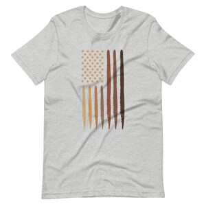 Op de afbeelding: Een heidekleurig T-shirt met een afbeelding van een Amerikaanse vlag. De vlag wordt weergegeven met een veld van witte sterren en rode en witte strepen. De strepen zijn vervangen door verschillende tinten bruin.